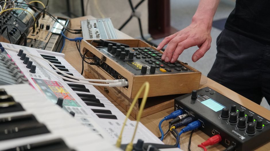 Close-up of a person adjusting electronic music equipment in a studio setting.
